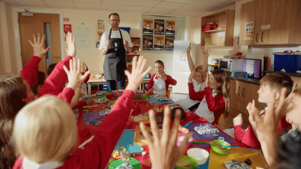 Children with hands up in a Curious Kids Club classroom session